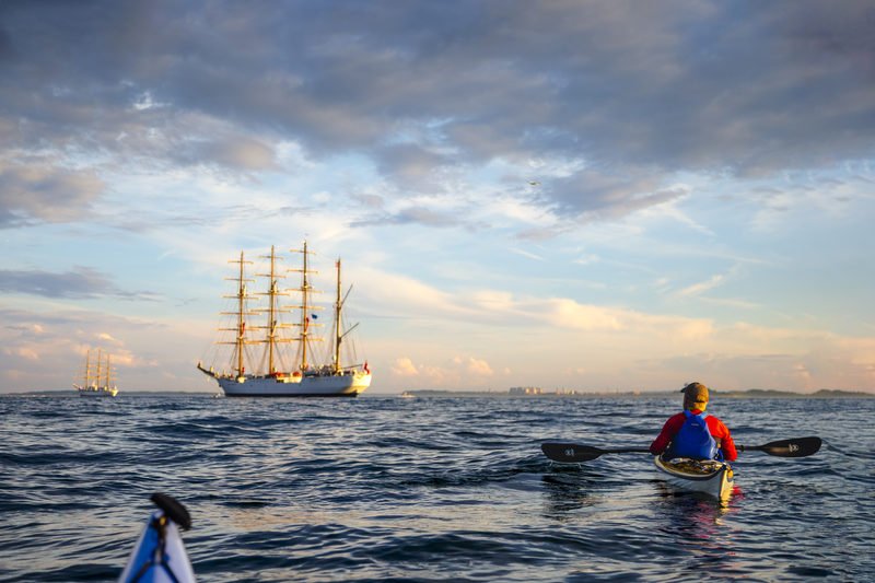 Kayaker paddling near a four-masted tall ship at sea