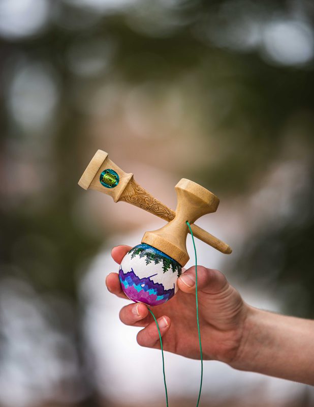 Hand holding a kendama toy mid-catch against a blurred forest background