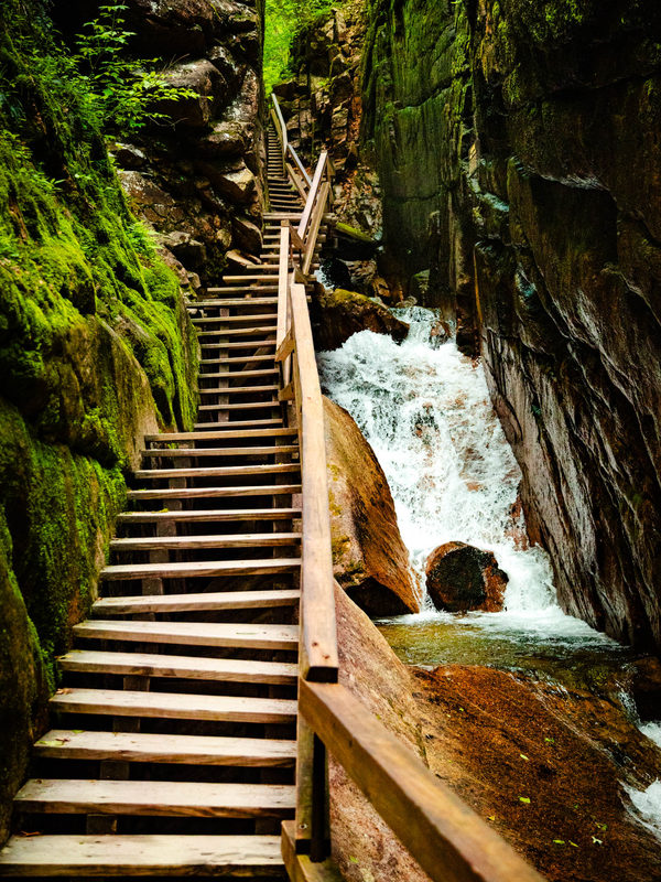 Wooden staircase beside a waterfall in the mossy granite walls of Flume Gorge