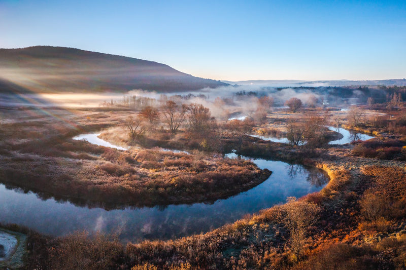 Aerial view of a foggy bend in the Housatonic River at golden hour among autumn foliage