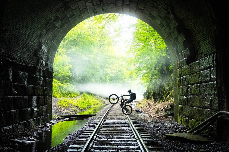Mountain biker popping a wheelie on railroad tracks inside a stone tunnel