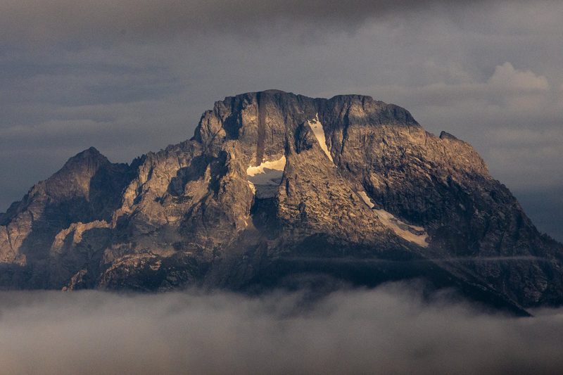 Rocky mountain peak emerging above a layer of clouds at golden hour