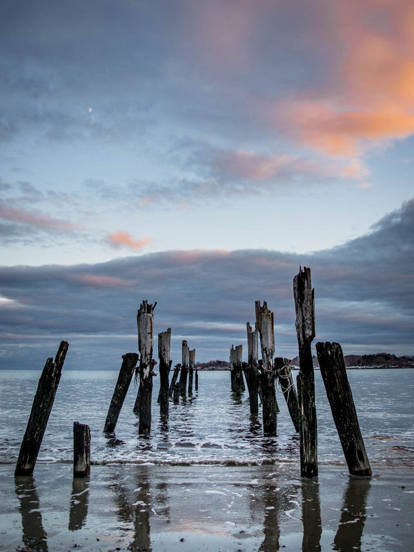 Old wooden pilings standing in shallow water at sunset on West Beach