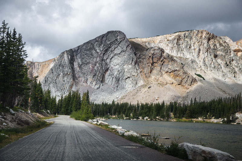 Gravel road along an alpine lake beneath granite peaks in Wyoming's Snowy Range under storm clouds